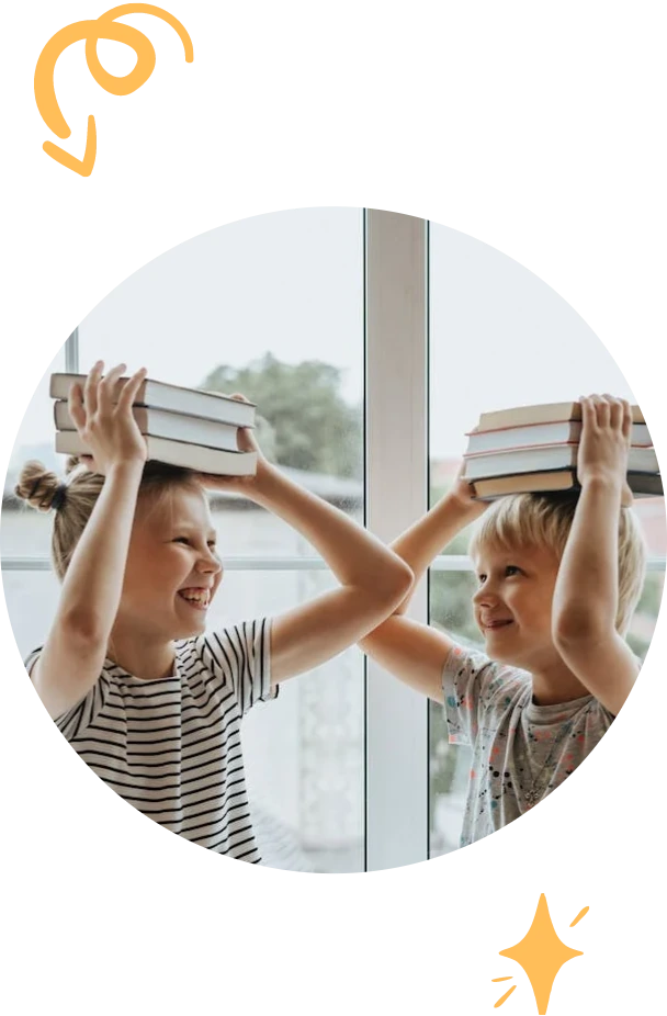 Two smiling children balancing stacks of books on their heads by a window