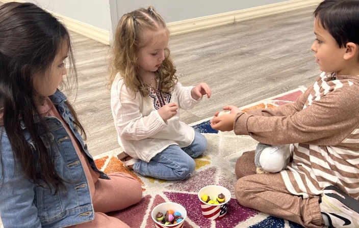 Three children sitting together on a colorful rug, playing and communicating during a group session